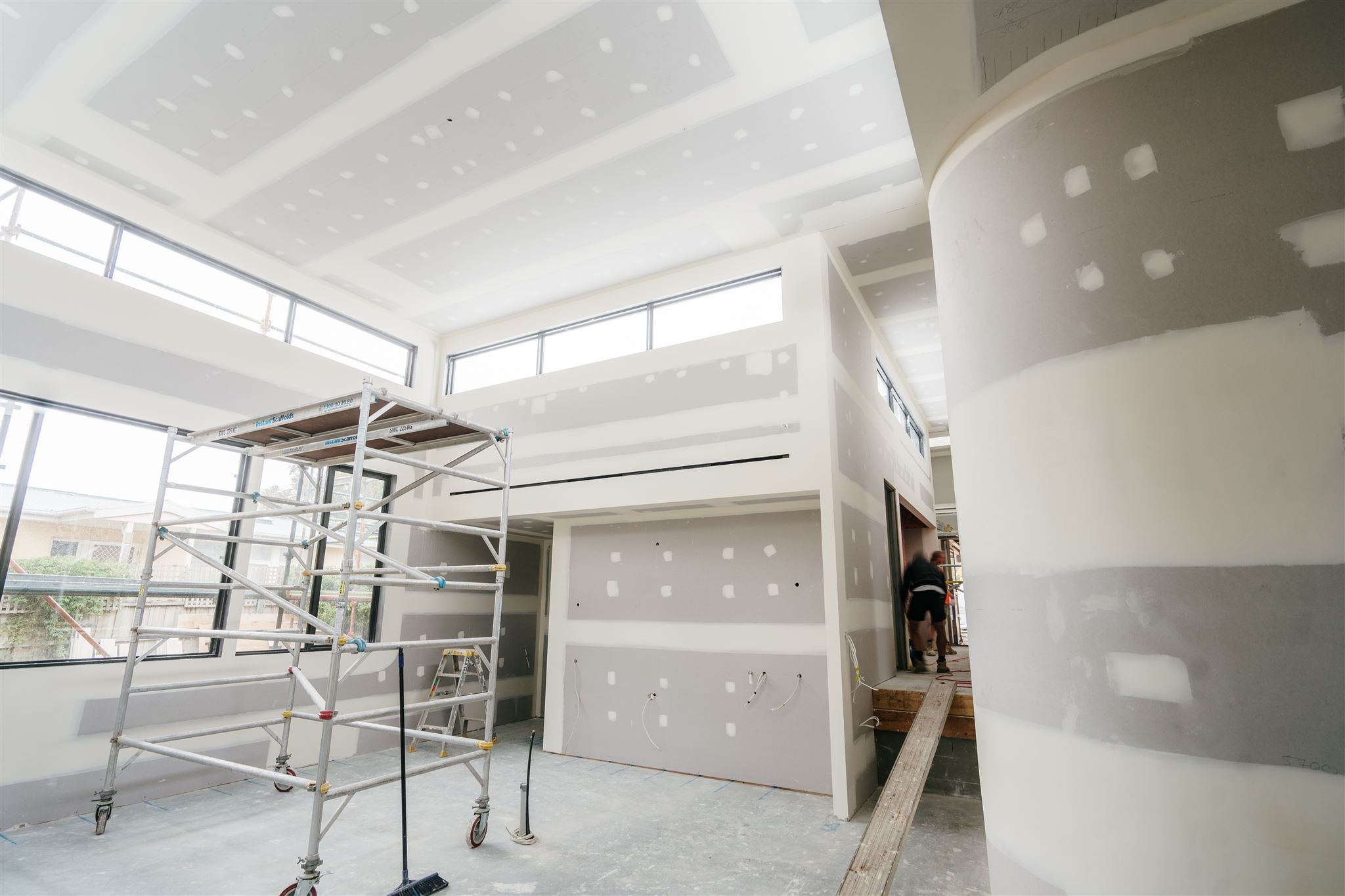 Mobile scaffold beside a curved plasterboard column, with a worker in the doorway behind