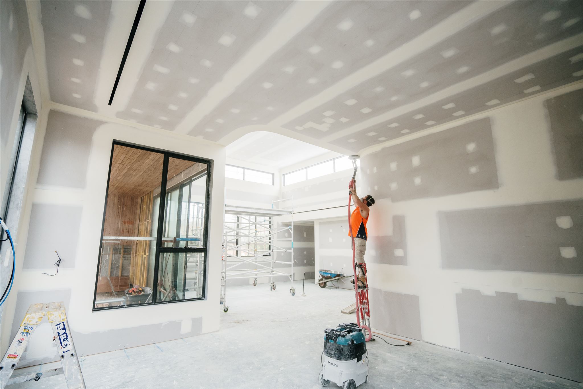 Plasterer on a ladder sanding the ceiling with a vacuum-connected sander