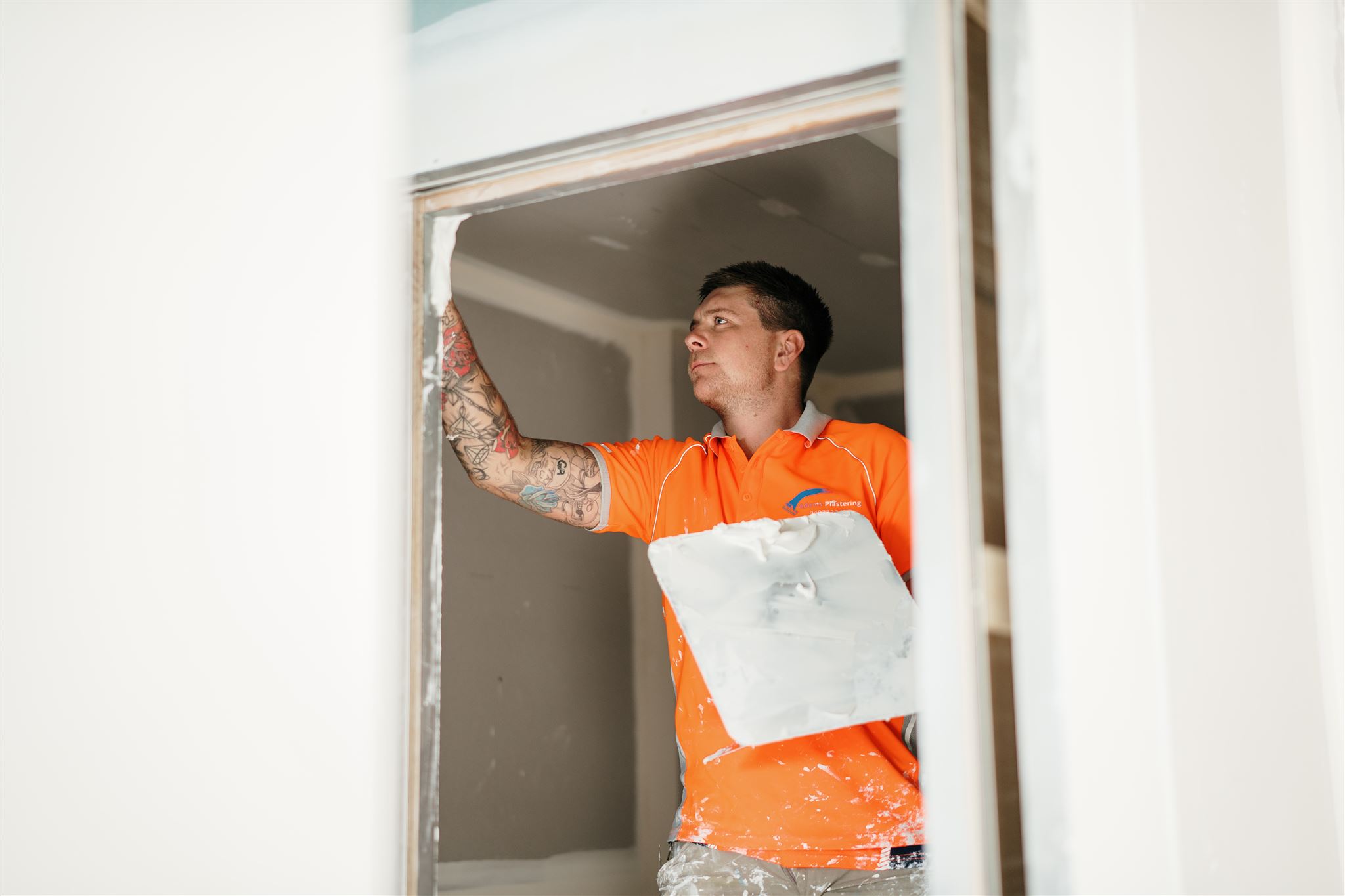 Plasterer in an orange work shirt holding a hawk while finishing plaster around an opening