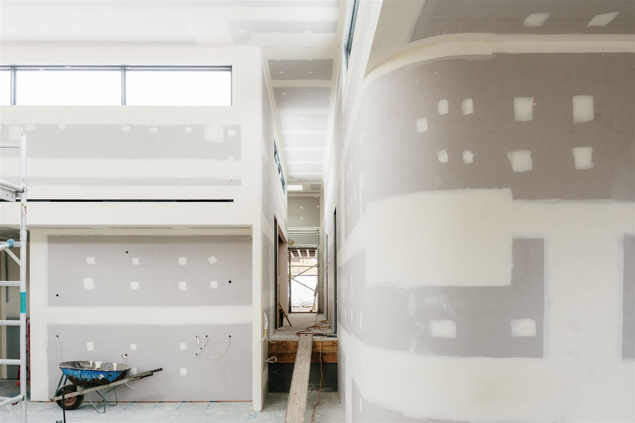Curved set plasterboard wall beside a corridor, with a wheelbarrow on the floor