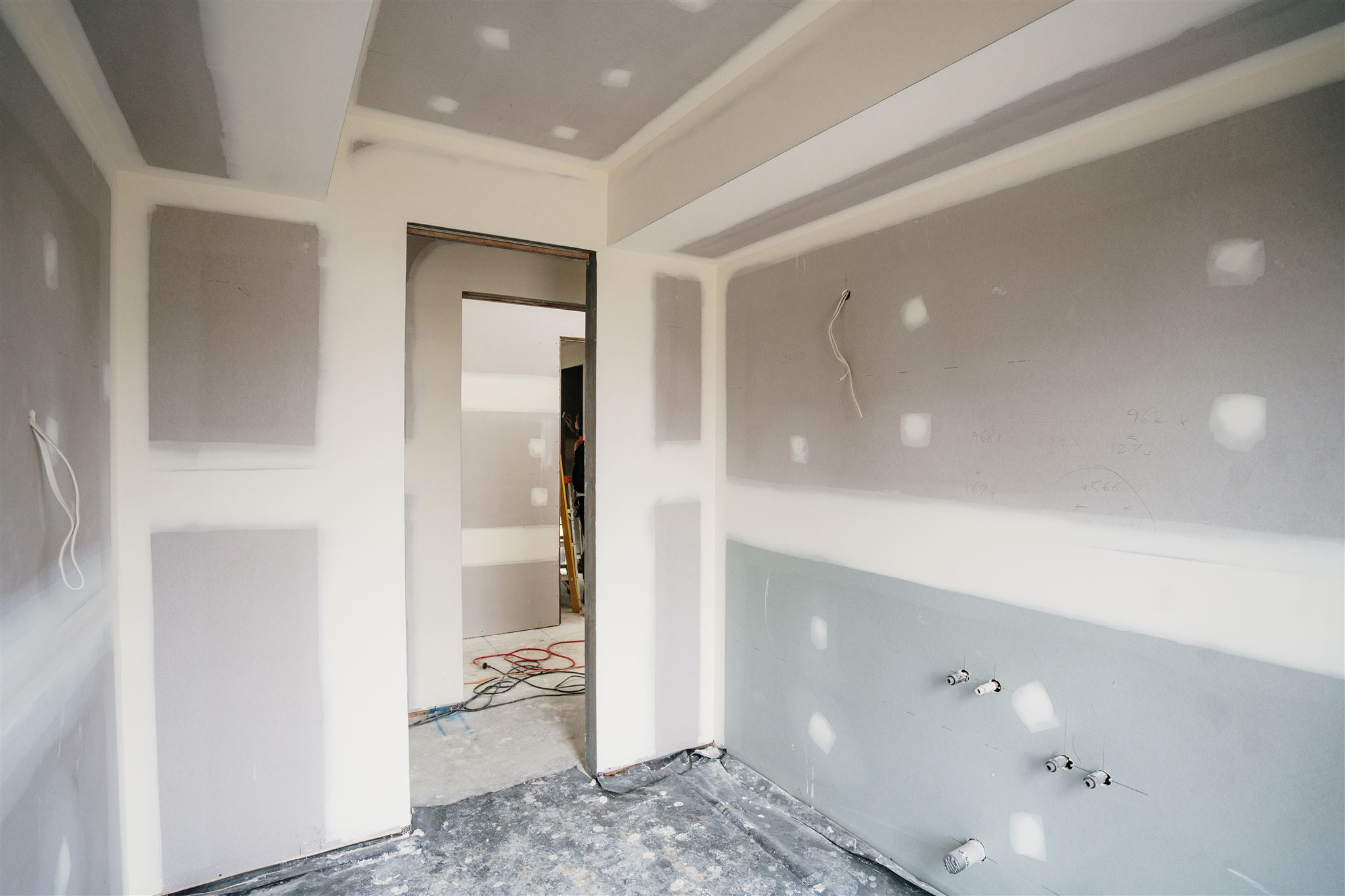 Small room with set plasterboard walls, plumbing outlets and plastic sheeting on the floor