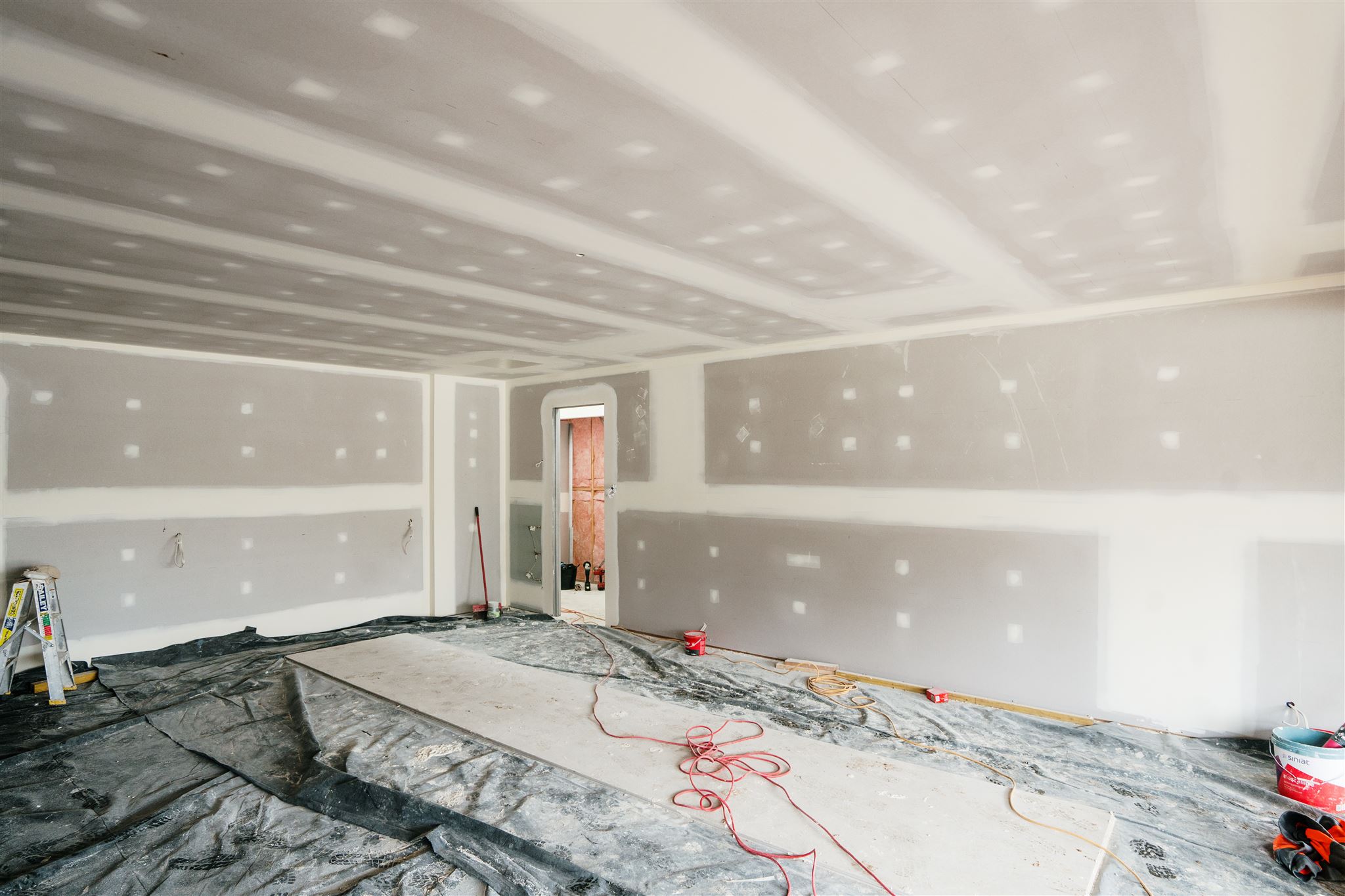 Large room with set plasterboard walls and ceiling, the floor covered in plastic sheeting